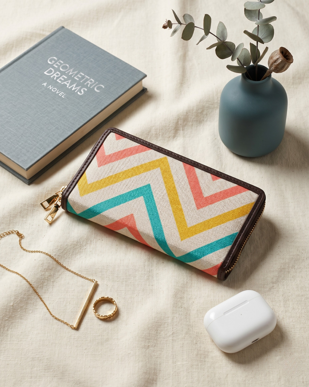 Colorful geometric-patterned pouch with a book, necklace, ring, and small plant on a beige surface.