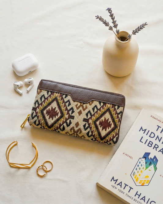 Patterned pouch, airpods, gold bracelet, ring, vase with lavender, and book on a light surface